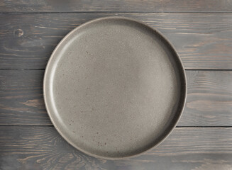 Empty rustic dark plate on a gray wooden background. Top view, with copy space.
