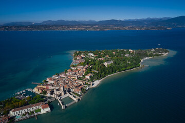 Obraz premium Top view of the town of Sirmione, Italy. Trees in the autumn season. Lake Garda, a tourist destination in northern Italy. Autumn in Italy on Lake Garda, Sirmione peninsula.