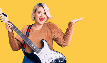 Fototapeta premium Young blonde plus size woman playing electric guitar celebrating victory with happy smile and winner expression with raised hands