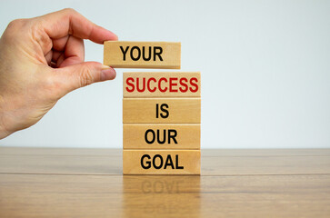 Wooden blocks with text 'your success is our goal'. Male hand. Beautiful wooden table, white background, copy space. Business concept.