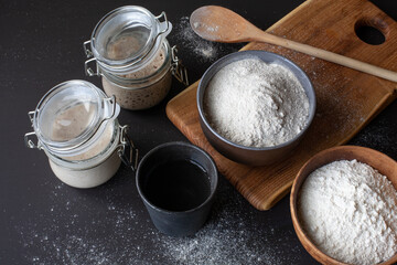 Active rye and wheat sourdough starter in glass jars with ingredients: flour and water. Top view.