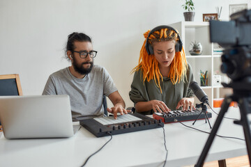 Woman with dreadlocks singing and playing. Female and male blogger making music using synthesizer, drum pad machine and laptop, recording video blog or vlog at home © Svitlana