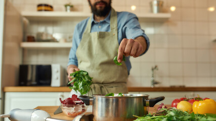 Cropped shot of man, chef cook adding basil leaf to the pot with chopped vegetables while preparing...