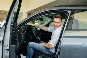 A young man is sitting in the cabin of a new car and testing it. Buying a car