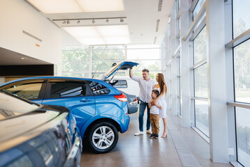 A happy young family chooses and buys a new car at a car dealership. Buying a new car