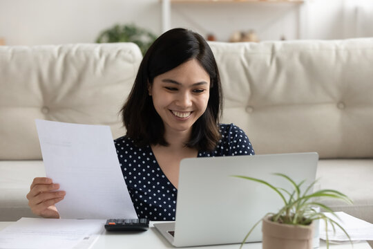 Smiling Young Vietnamese Woman Look At Laptop Screen Paying Bills Taxes Online Use Easy Banking System. Happy Asian Female Manage Budget At Home, Consider Household Finances Expenditures On Computer.