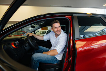 Fototapeta na wymiar A young man is sitting in the cabin of a new car and testing it. Buying a car