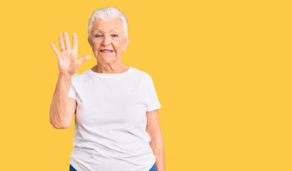 Senior beautiful woman with blue eyes and grey hair wearing casual white tshirt showing and pointing up with fingers number five while smiling confident and happy.