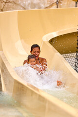 Young mother with her son rides down a hill in a water park