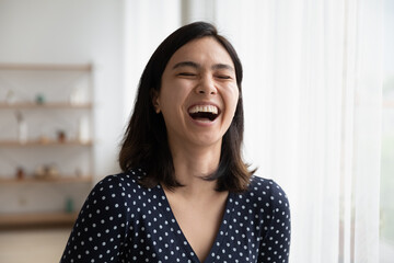 Close up of overjoyed young asian woman laugh at good funny joke indoors. Happy smiling millennial...