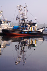 Colorful, weathered fishing boat in a marina on a foggy day
