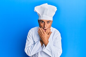 Mature middle east man wearing professional cook uniform and hat shocked covering mouth with hands for mistake. secret concept.