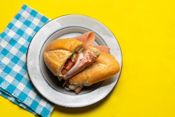 Mexican ham sandwich with avocado and cheese also called torta on yellow background