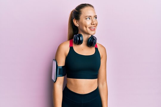 Beautiful young blonde woman wearing gym clothes and using headphones looking to side, relax profile pose with natural face and confident smile.