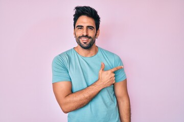 Fototapeta premium Handsome hispanic man with beard wearing casual clothes cheerful with a smile of face pointing with hand and finger up to the side with happy and natural expression on face