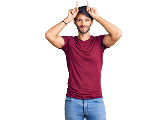 Handsome hispanic man wearing casual clothes doing funny gesture with finger over head as bull horns