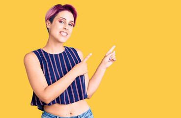 Young beautiful woman with pink hair wearing casual clothes smiling and looking at the camera pointing with two hands and fingers to the side.