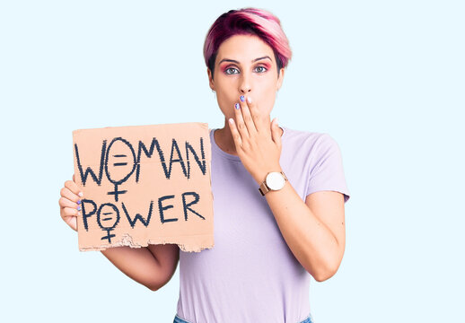 Young beautiful woman with pink hair holding woman power banner covering mouth with hand, shocked and afraid for mistake. surprised expression