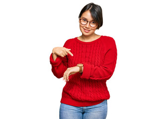 Young beautiful hispanic woman with short hair wearing casual sweater and glasses in hurry pointing...