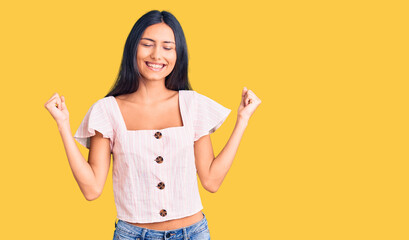 Young beautiful latin girl wearing casual clothes very happy and excited doing winner gesture with arms raised, smiling and screaming for success. celebration concept.