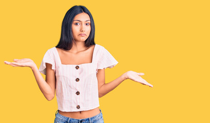 Young beautiful latin girl wearing casual clothes clueless and confused expression with arms and...