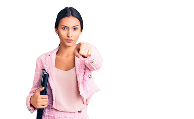 Young beautiful latin girl wearing business clothes holding binder pointing with finger to the camera and to you, confident gesture looking serious