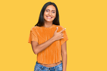 Young brunette arab woman wearing casual clothes cheerful with a smile of face pointing with hand and finger up to the side with happy and natural expression on face