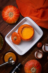 Fototapeta na wymiar baked pumpkin cream coup served in pumpkin. served at wooden brown table with ripe orange pumkins. flat lay. healthy life concept