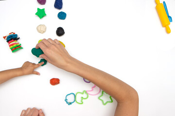 Toddler sculpts from colored plasticine on a white table. The hand of a small child squeezes pieces of colored plasticine.