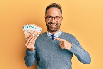 Handsome middle age man holding bunch of 50 euro banknotes smiling happy pointing with hand and...