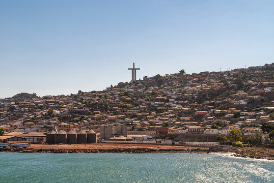 Coquimbo, Chile - December 7, 2008: Tall Millennium Cross Trinity surrounded by houses in different colors under blownish cloudscape towers over harbor site and azure ocean water..