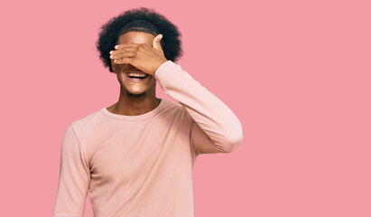 Fototapeta na wymiar African american man with afro hair wearing casual clothes smiling and laughing with hand on face covering eyes for surprise. blind concept.