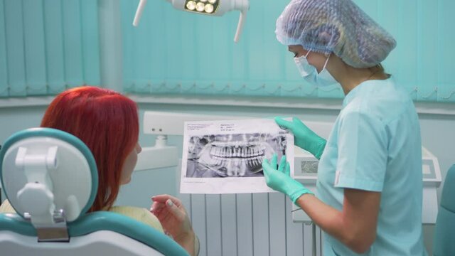 A young woman dentist shows a panoramic x-ray of the jaw to a patient in a dental clinic. Steadicam shot.