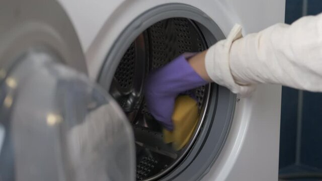 Disinfect the washing machine. A female wearing gloves washes the washing machine.