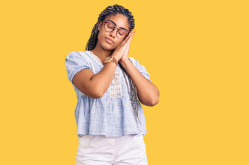 Young african american woman with braids wearing casual summer clothes and glasses sleeping tired dreaming and posing with hands together while smiling with closed eyes.