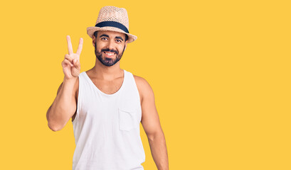 Naklejka premium Young hispanic man wearing casual summer hat showing and pointing up with fingers number two while smiling confident and happy.