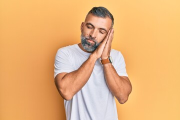 Middle age handsome man wearing casual white tshirt sleeping tired dreaming and posing with hands together while smiling with closed eyes.