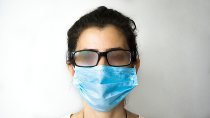 A woman standing with smoky glasses and a mask on white background. Female can't see because of her...