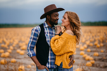 An African man and a Caucasian woman are standing embracing in a pumpkin field and looking at the camera. Close-up portrait.