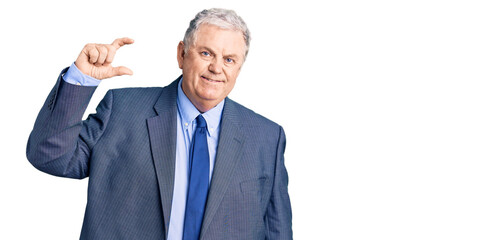 Senior grey-haired man wearing business jacket smiling and confident gesturing with hand doing small size sign with fingers looking and the camera. measure concept.