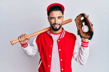 Young man with beard playing baseball holding bat and ball winking looking at the camera with sexy...