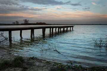 Obraz premium Wooden bridge towards the lake and dark evening clouds