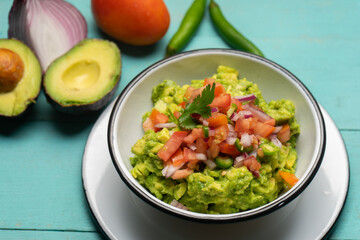Mexican guacamole with chili pepper and tomato on turquoise background