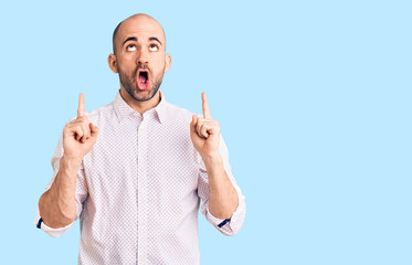 Naklejka premium Young handsome man wearing elegant shirt amazed and surprised looking up and pointing with fingers and raised arms.