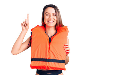 Obraz na płótnie Canvas Young beautiful girl wearing life jacket surprised with an idea or question pointing finger with happy face, number one