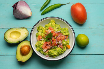 Mexican guacamole with chili pepper and tomato on turquoise background