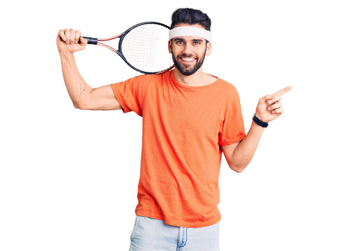 Young handsome man with beard playing tennis holding racket smiling happy pointing with hand and finger to the side