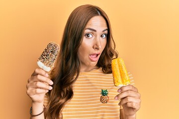 Young brunette woman wearing summer style holding ice cream in shock face, looking skeptical and...