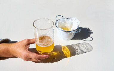 Girl's hand picks up the glass of beer with the shadow reflected on the white table and with sun shine reflected in the shadow