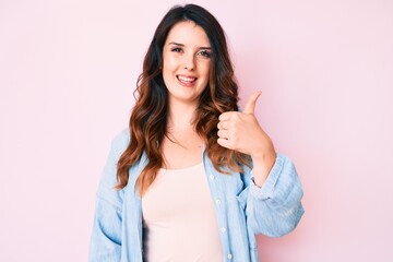 Young beautiful brunette woman wearing casual clothes over pink background smiling happy and positive, thumb up doing excellent and approval sign